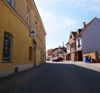 A street in Trnava with dining spaces, yellow and brick buildings, parked car.