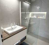 Bathroom with a sink, glass shower enclosure, and light tiles in a 2-room apartment.