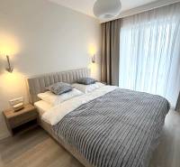 Bedroom in a two-room apartment with wood-patterned flooring, a bed, and curtains.
