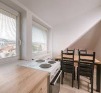 A kitchen in a 2-room apartment with a stove, microwave, and dining table, with a view of the city.