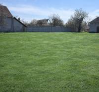 A garden in Dolná Seč surrounded by family houses and fencing under a blue sky.