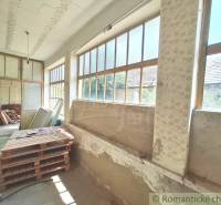 A cottage with a spacious veranda, large windows, and a variety of stored materials.