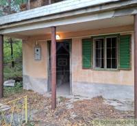 A cottage in Kamenín with a veranda and green shutters surrounded by nature.