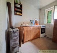 The interior of a cottage with a simple kitchen unit, a stove, and an open window.
