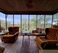 Interior of a cabin with comfortable armchairs and a view of trees through large windows.