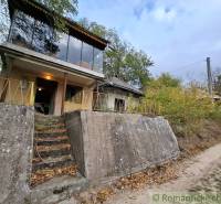 A cottage in Kamenín surrounded by greenery, with large windows and a concrete front entrance.
