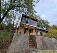 A cottage in Kamenín with a concrete foundation and large windows amidst trees.