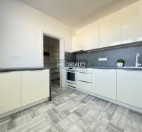 A kitchen in a 2-room apartment with a grey floor featuring a wooden design and white cabinets.