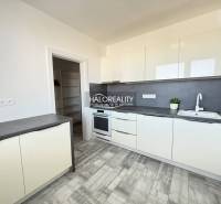 A kitchen in a 2-room apartment with white furniture and a wooden decor floor.
