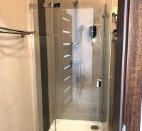 Shower corner with a glass screen in a studio apartment with soft beige tiles.