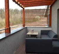 A balcony of a 2-room apartment with wooden decor and a view of greenery.