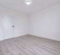 An empty room in a 3-room apartment with wood-patterned flooring and white walls.