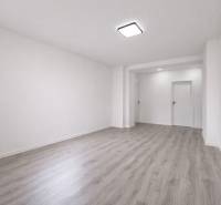 A spacious room in a 3-room apartment with wood-patterned flooring and white walls.