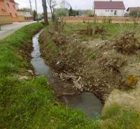 A stream near residential plots in Horná Kráľová surrounded by greenery and trees.