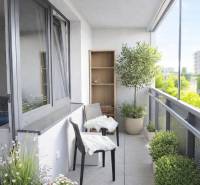 A balcony of a 2-room apartment with plants and two chairs, view of greenery.