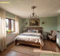 A bedroom with rustic furniture, a wooden decor floor, and a large window in a family house.