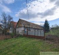 A family house in Ozdín, surrounded by a garden and trees, under a blue sky.