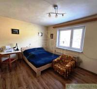 A bedroom with a bed, table, and chair in a family house. The floor has a wooden decor.