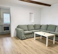 Living room with a corner sofa, wood-patterned flooring, and a kitchen in a family house.