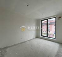 A room in a 2-room apartment with a raw floor and a large window overlooking the street.