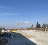 A building and exterior with an empty lot, blue sky, trees in the background.