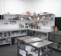 Professional kitchen with stainless steel surfaces, shelves, and kitchen equipment, floor with wooden decor.