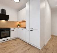 A kitchen with light furniture and a wooden decor floor in a 2-room apartment.