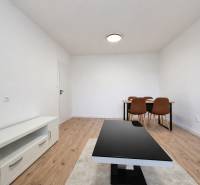 A room in a 2-room apartment with a wooden decor floor, a table, and chairs.