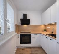 A kitchen of a two-room apartment with a wooden decor floor and white cabinets.