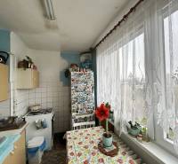 A kitchen of a three-room apartment with a large window, a curtain, and flowers on the windowsill.