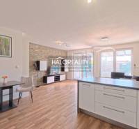 A bright living room in a two-room apartment with wood-patterned flooring and a kitchen island.