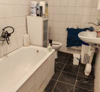 A bathroom in a family house with a bathtub, a sink, and tiles with a dark pattern.
