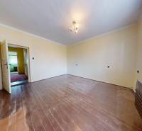 A room with a wooden floor decor, light-colored walls, and a window with a white curtain.