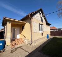 A family house in Belince with a front garden and a concrete yard under a blue sky.