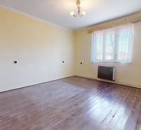 An empty room in a family house with a wood-patterned floor and yellow walls.