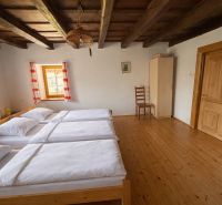 A room in a family house with a wooden ceiling, three beds, and a floor with a wooden decor.