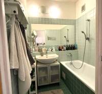 Bathroom in a 3-room apartment with a bathtub, sink, green tiles, and shelves.
