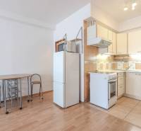 A kitchen in a 2-room apartment with a wood-patterned floor, a dining table, and a refrigerator.