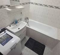 Bathroom with a bathtub and a washing machine in a studio apartment, light tiles and storage space.