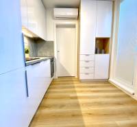 A kitchen with white cabinets and a wood-patterned floor in a two-room apartment.