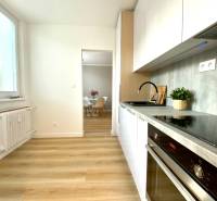 A kitchen in a 2-room apartment with white cabinets and a wood-patterned floor.