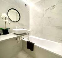 A bathroom in a 2-room apartment with a bathtub, a mirror, and floral decoration.