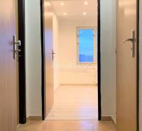 A hallway with ceramic tiles and an entrance to a room with a wooden decor floor.