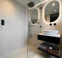 A bathroom in a family house with an illuminated mirror, a glass shower enclosure, and a sink.