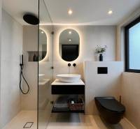 A bathroom in a family house with an oval mirror, a sink, and a black shower enclosure.