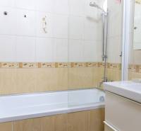 Bathroom with tiles and a bathtub in a 4-room apartment, light colors and a shower head.