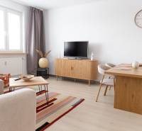 Living area of a 4-room apartment with a TV, sofa, table, and floor with wooden decor.