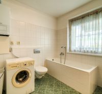 A bathroom in a 3-room apartment with a washing machine, a bathtub, and a window, tiled walls.