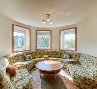 Round room in a 3-room apartment with a sofa, a central table, and windows with a view.