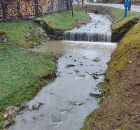 A stream flowing through recreational lands in Púchov with wood stored on the edge.